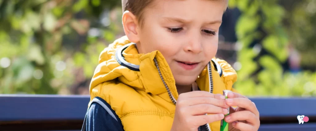 Photo of a little boy sitting on a park bench unwrapping a pack of chewing gum with a joyful and looking forward expression on his face dressed in a yellow vest in a nature background | Source: shutterstock.com | For the article: 7 interesting facts about chewing gum | For Website: HealthChewingGum.com (Healthy Gums)