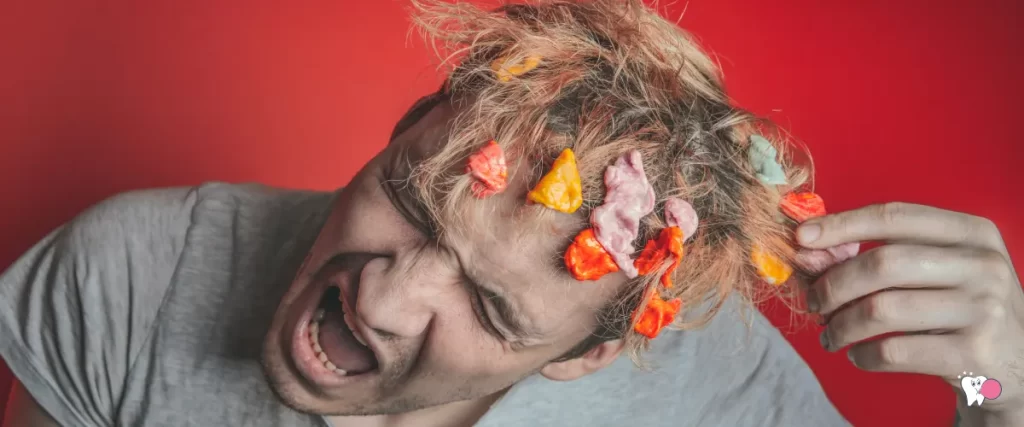 Photo of a man with chewing gum in his hair tearing one stuck in his hair against a red background | Source: shutterstock.com | For Article: Controversial Chewing Gum Ingredients | For website: Healthy Chewing Gum (healthchewinggum.com)