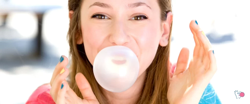 A young girl (woman) blowing a bubble gum with a joyful look in the foreground, her face with her hands as the main subject | Source: shutterstock.com | For Website: HealthChewingGum.com | For the article: The main reasons for chewing