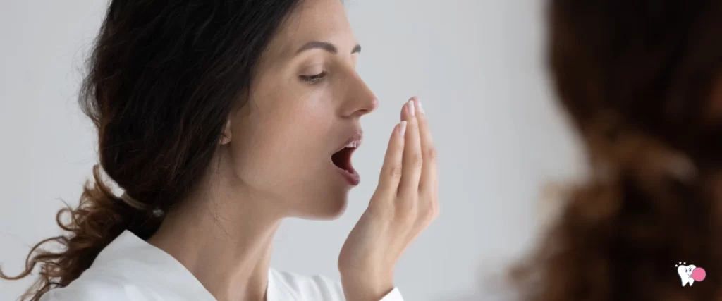 Photo of young lady in white t-shirt breathing into left palm of hand detecting bad breath gray background | Source: shutterstock.com | Article: Bad breath | For website: healthchewinggum.com